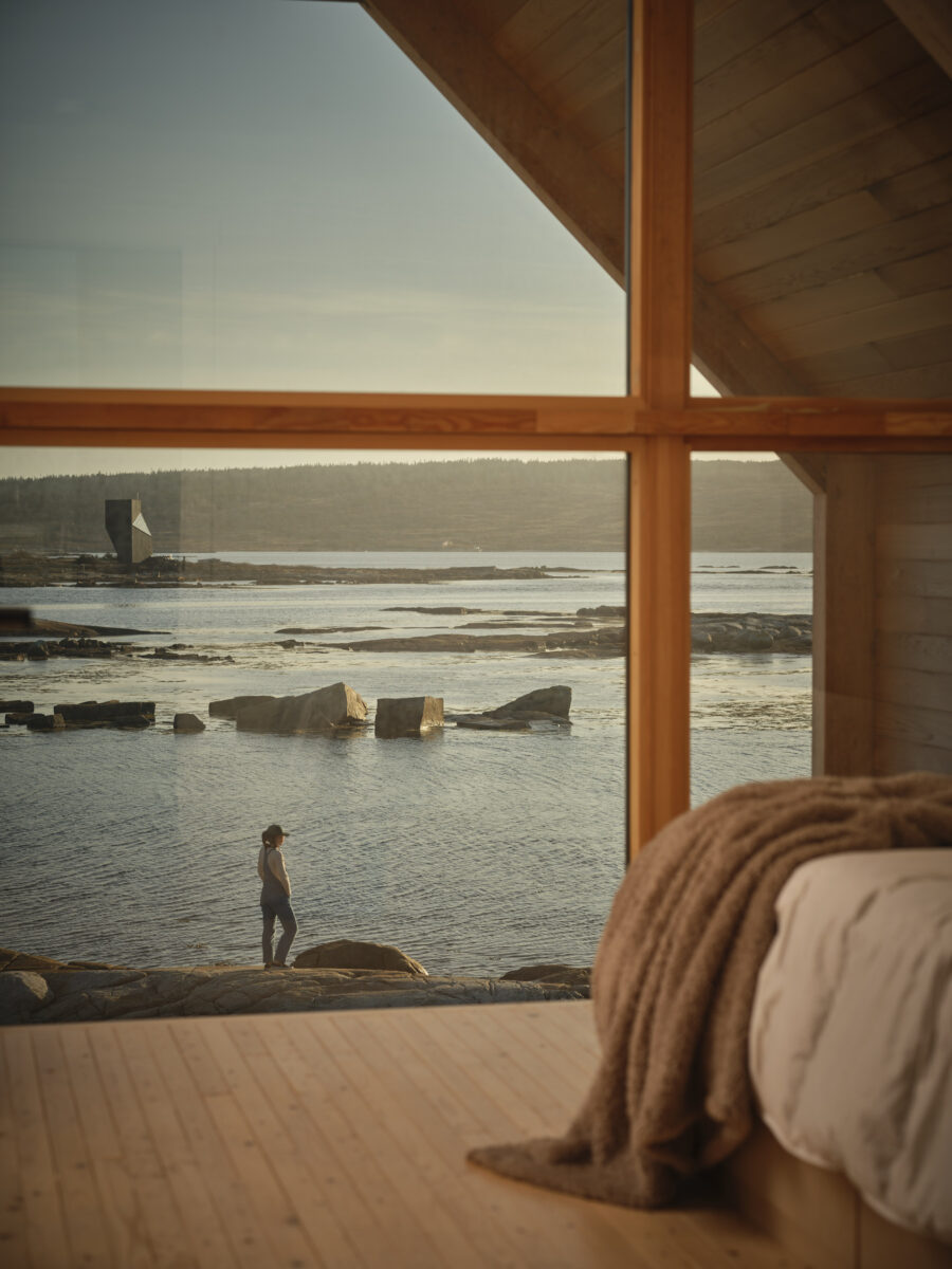 Interior image of an assembled Backcountry Huts Company cabin on Fogo Island, showing the warmth of the wood inside the cabin, with the view outside the window off the rocky coastline of Newfoundland
