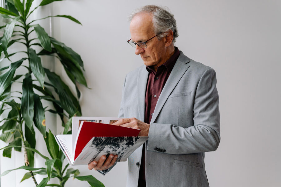 Paul Fast, founder of Fast + Epp, stands in front of a wall and plant while flipping through his book, Design Trails.
