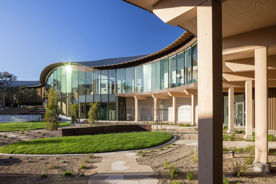 Exterior shot of Ohana Montage Health Facility, showing a close up of the curved building and it's timber columns that support the overhang below the expansive windows.